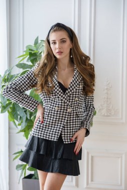 Gayri resmi takım elbiseli güzel bir manken ve yüksek topuklu ayakkabılar tencerede yeşil bir fabrikanın yanında duruyor. 