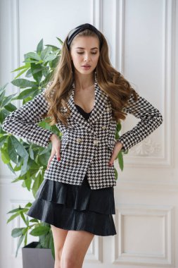 Gayri resmi takım elbiseli güzel bir manken ve yüksek topuklu ayakkabılar tencerede yeşil bir fabrikanın yanında duruyor. 