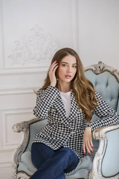 豪華なアパートのインテリアでアームチェアに座ってカジュアルな服で美しい若い女性の肖像画 — ストック写真