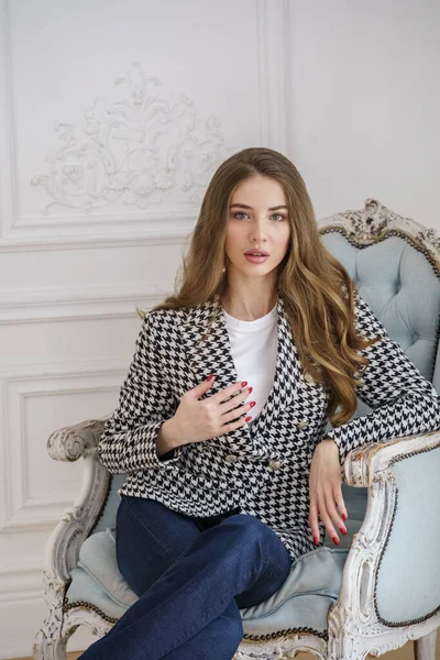 Portrait of beautiful young woman in casual clothes sitting in armchair at luxury apartments interior