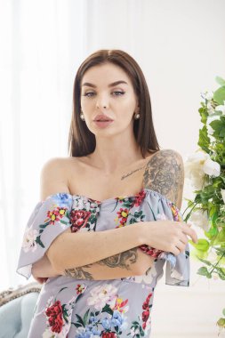 Renkli yaz elbiseli güzel esmer kadın lüks dairelerde beyaz çiçeklerin yanında poz veriyor. 