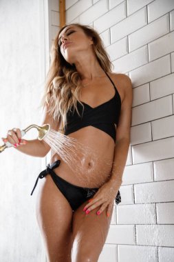 Siyah iç çamaşırlı çekici genç manken duş odasının iç tarafında beyaz fayans duvarının yanında duruyor.