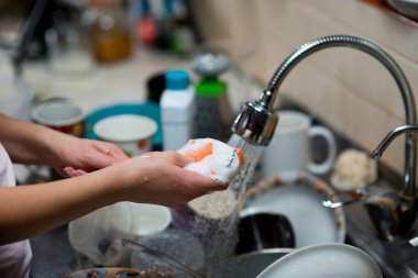 Kız kirli tabaklarla lavabonun arka planına çatal sürüyor.