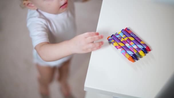 一个小女孩从架子上拿出一支蜡笔 立刻开始画在一个白色的架子上 — 图库视频影像