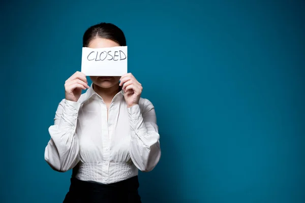 Young woman in white shirt and glasses covers her face with a piece of paper with the inscription closed — Stock Photo, Image