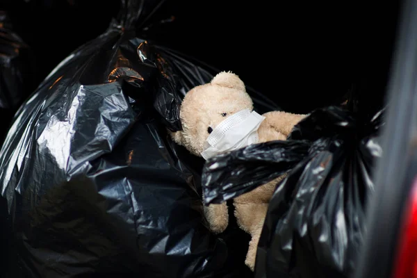 Un oso de peluche con un vendaje médico en la cara se encuentra en las bolsas de residuos — Foto de Stock