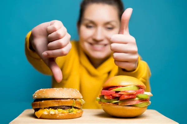 Το κορίτσι δίνει ένα διαφορετικό σήμα για το κρέας και χορτοφαγικό burger, επιλέγοντας υγιή — Φωτογραφία Αρχείου