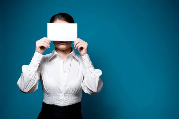 Woman in white shirt and glasses covers her face with a blank sheet of paper — Stock Photo, Image