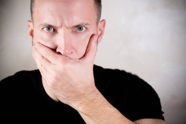 Sert bakışlı bir adam avuçlarıyla ağzını kapatır.