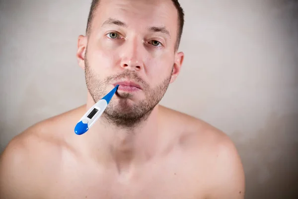 Ongeschoren man zonder kleren houdt een thermometer in zijn mond en kijkt nieuwsgierig — Stockfoto