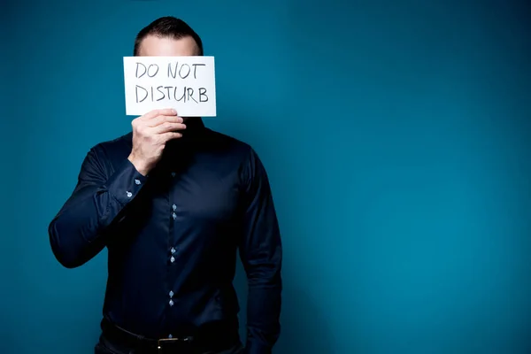 En man i blå skjorta täcker sitt ansikte med en inte störa tecken — Stockfoto