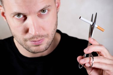 Tıraşsız adam bir sigarayı makasla kesecek.
