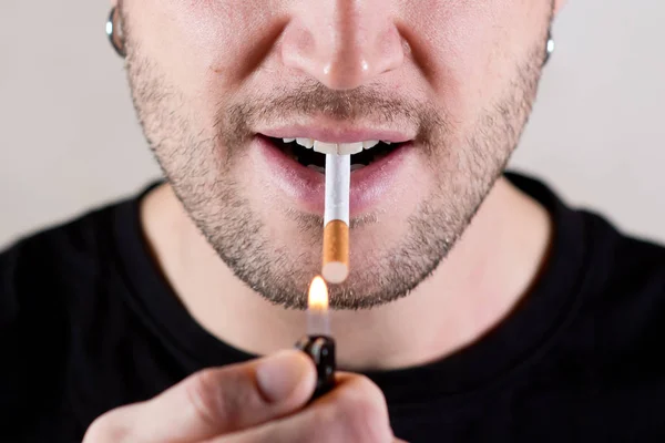 사람들은 담배에 불을 붙이려고 하고 있으며, 그것을 그릇된 면으로 입에 넣고 있다. 눈 이 없으면 얼굴 의절 반 이 낮아 진다 — 스톡 사진
