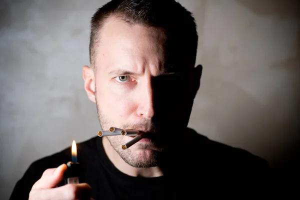 En man med ett halvljust ansikte ser skeptisk ut och cigaretter sticker ut ur munnen — Stockfoto