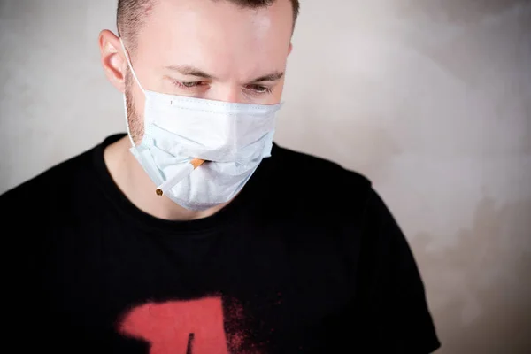 Ένας άντρας με ιατρική μάσκα έχει ένα τσιγάρο στο στόμα του. — Φωτογραφία Αρχείου
