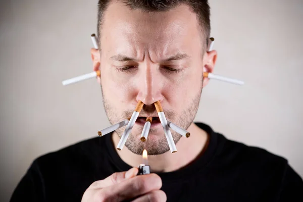 Um homem sem barba está prestes a acender um cigarro, enquanto cigarros saem do nariz e ouvidos — Fotografia de Stock