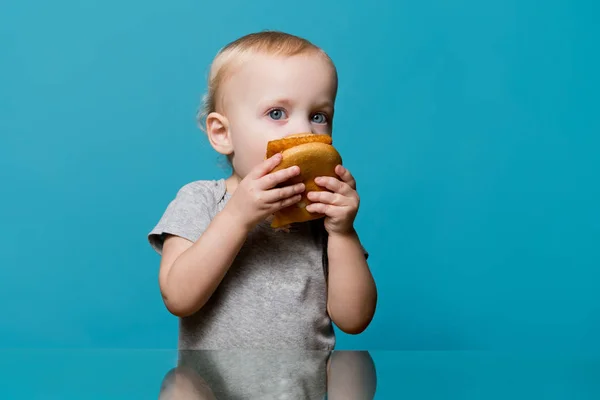 Dziewczynka nieudolnie próbuje ugryźć hamburgera i patrzy w kamerę — Zdjęcie stockowe