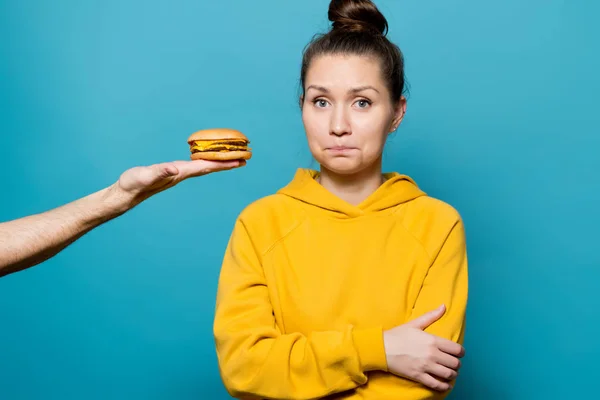 Meisje in een helder sweatshirt met moeite beperkt de verleiding om te proberen een hamburger — Stockfoto