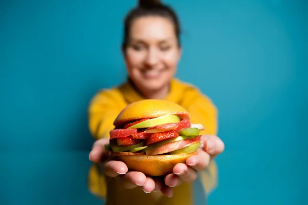 Een hamburger van vruchten en bessen ligt op de handen van een meisje dat onscherp is — Stockfoto