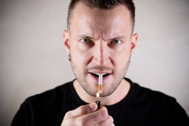 Tıraşsız yakışıklı bir adam sigarasını yakmak üzere, yanlış tarafıyla ağzına alıyor.