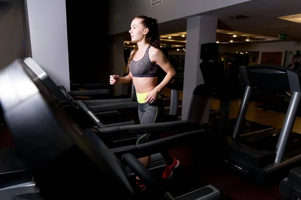 Chica corre en una cinta de correr solo en un club deportivo —  Fotos de Stock