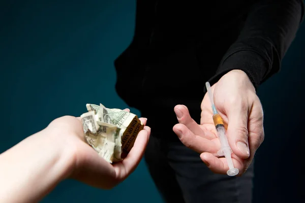 hand holds out crumpled dollars in exchange for a syringe with a dose of drug