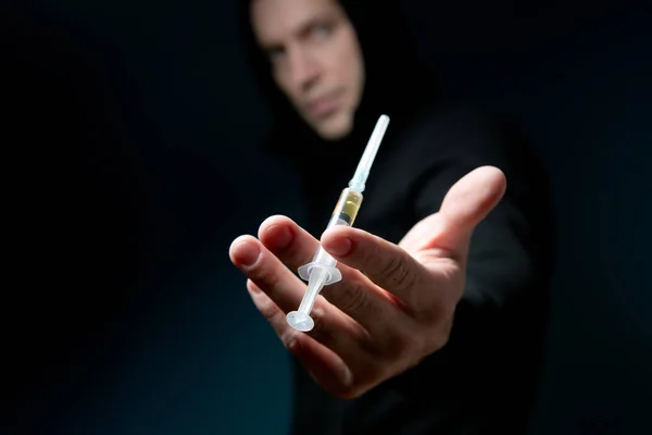 Hombre mira fuera de la oscuridad sosteniendo una jeringa con una droga — Foto de Stock