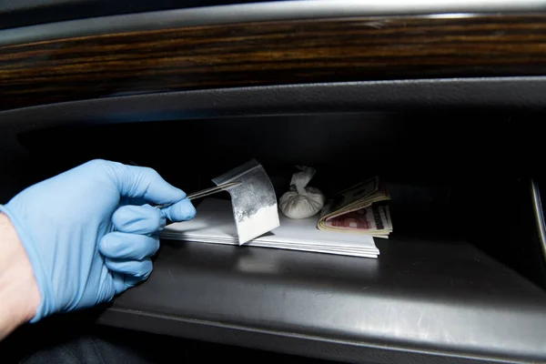Una mano con guantes saca pinzas de cocaína de la guantera de un coche . — Foto de Stock