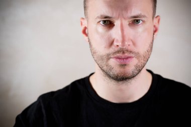 Üç gün sakallı, genç ve yakışıklı bir adam duygusuzca kameraya bakıyor.