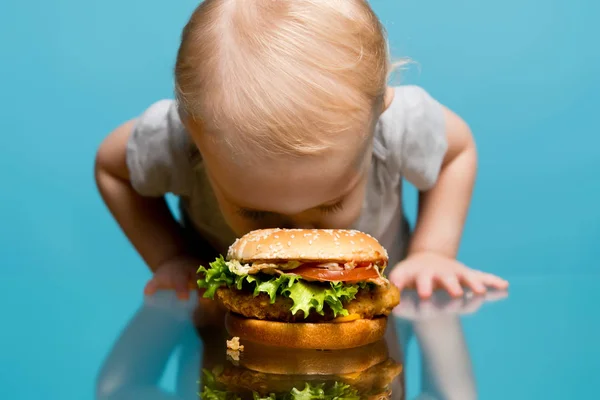 Dziewczynka zakopała twarz w hamburgerze leżącym na stole — Zdjęcie stockowe