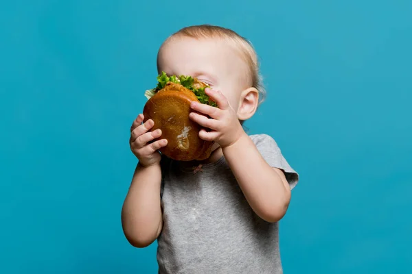 Mała dziewczynka entuzjastycznie gryzie lub wącha hamburgera wielkości jej twarzy — Zdjęcie stockowe