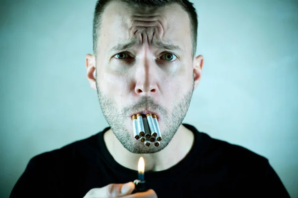Un hombre con cara de sufrimiento tiene muchos cigarrillos en la boca y mira a la cámara — Foto de Stock