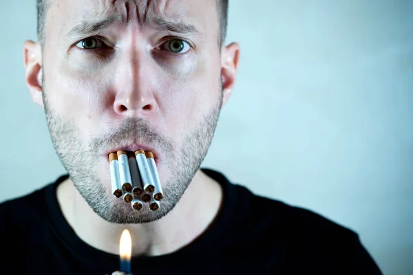 En man med ett lidande ansikte håller en hel del cigaretter i munnen och tittar på kameran, kopiera utrymme — Stockfoto