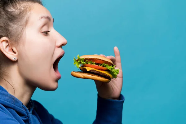 Het meisje doet haar mond wijd open en gaat een hamburger eten. — Stockfoto