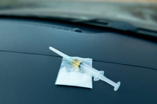 Una jeringa y una bolsa con una dosis de la droga se encuentran en el salpicadero del coche — Foto de Stock