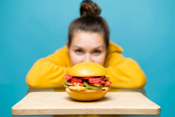 Jonge vrouw kijkt naar een veggie burger liggend in de voorkant van haar — Stockfoto