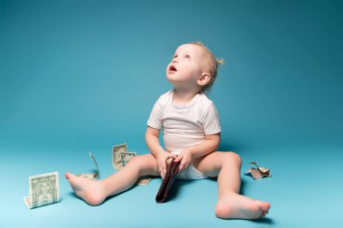 Küçük kız annesinin cüzdanını elinde tutarak yukarı bakıyor. Etrafa saçılmış dolar