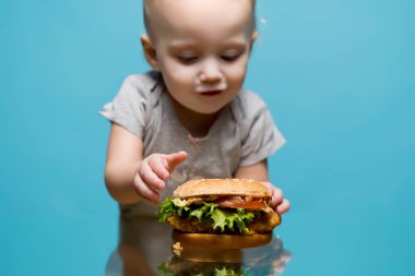 Küçük çocuk masadan bir hamburger alacak.
