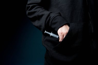 Bir kadın eli, bir şırıngayı cebinden aldığı uyuşturucuyla yakın plan çeker..