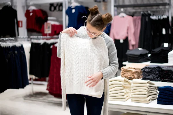 Junge Frau in einem Bekleidungsgeschäft wählt einen Pullover — Stockfoto