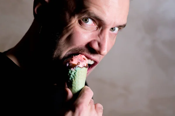 Unshaven man with a stern look bites an ice cream in a waffle cone — Stockfoto