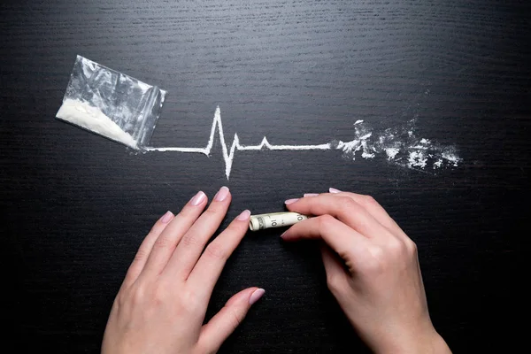 Mãos femininas, dólar e cocaína na forma de uma linha de batimentos cardíacos — Fotografia de Stock