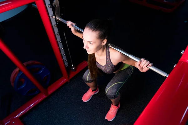 Kız ve çömelme makinesi spor salonunda. — Stok fotoğraf