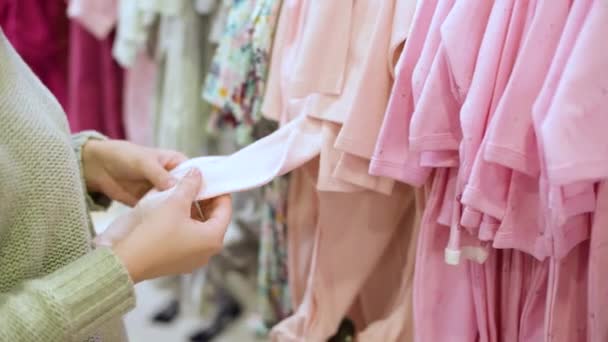若い女性は子供服屋で子供用の服を選ぶ生地を感じ 品質をチェックする — ストック動画