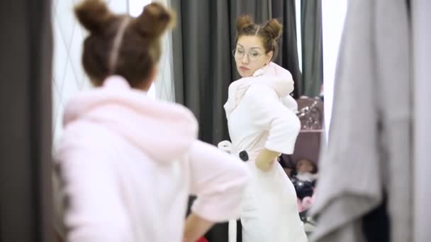 Mädchen Probiert Einem Bekleidungsgeschäft Einen Bademantel Untersucht Sich Selbst Spiegel — Stockvideo