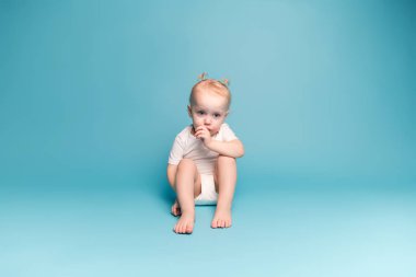 Küçük kız parmağını emiyor, aşağı bakıyor.