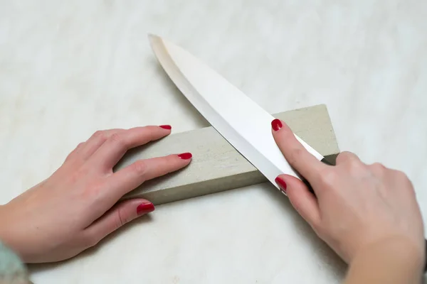 Mulher solitária afiando uma faca em uma grindstone na cozinha — Fotografia de Stock