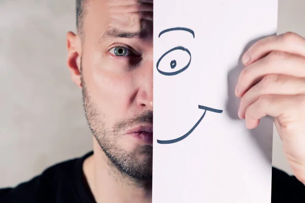 Una sonrisa pintada sobre papel cubre parcialmente la cara de un hombre triste — Foto de Stock