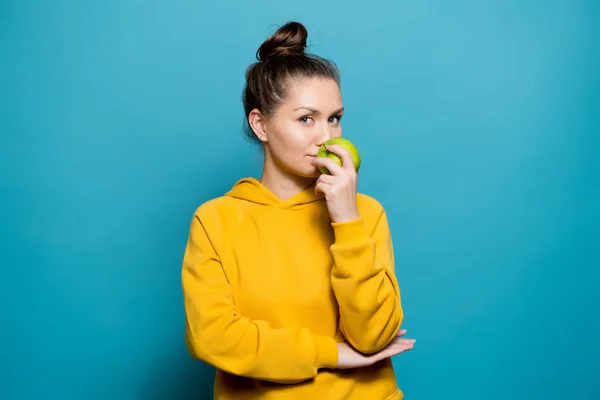 Kalm meisje in een helder sweatshirt ruikt een frisse groene appel — Stockfoto