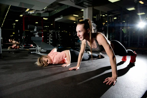 Atletisk flicka utför armhävningar i gymmet medan hennes vän redan är utmattad — Stockfoto